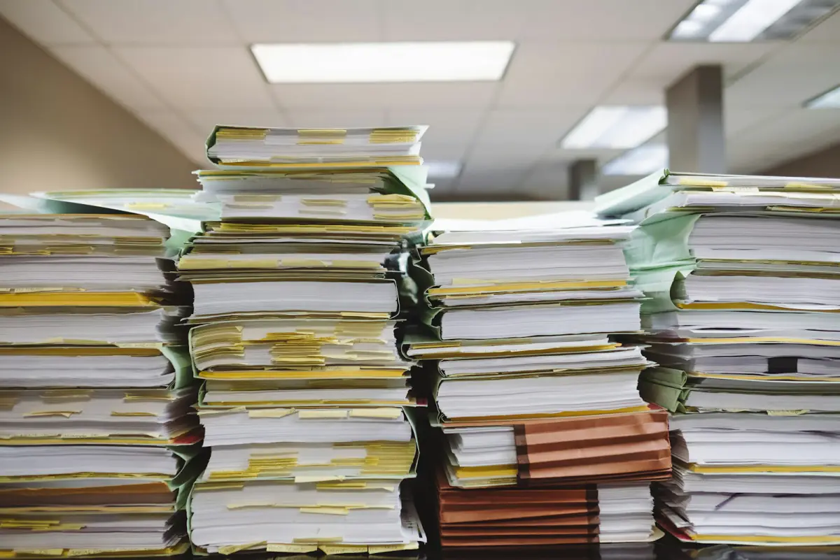 Hohe Stapel aus Akten und Ordnern auf einem Bürotisch.